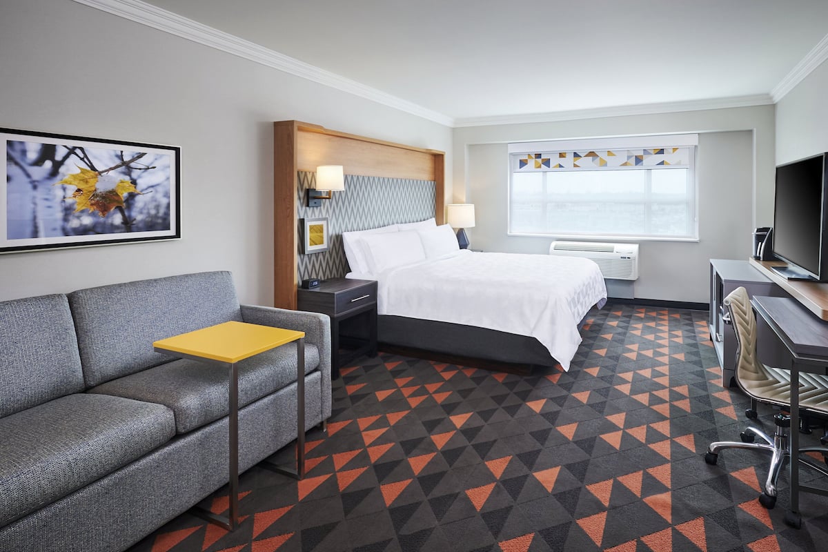 A hotel room with a bed, a sofa, a desk, a TV, and a window with a view.