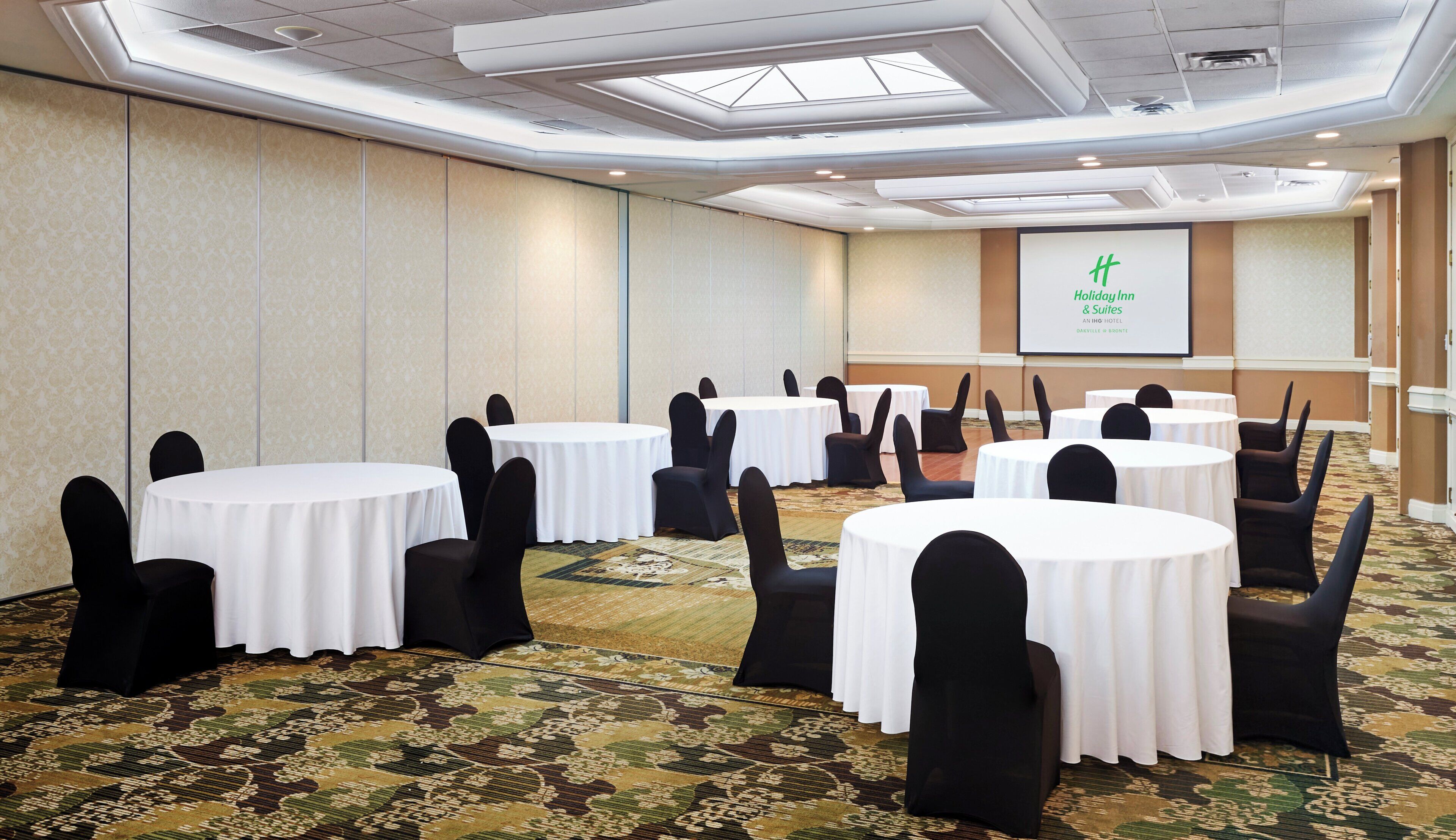 Une salle de conférence avec des tables rondes, des chaises noires et un sol recouvert de moquette.