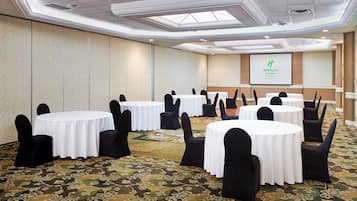 Une salle de conférence avec des tables rondes, des chaises noires et un sol recouvert de moquette.