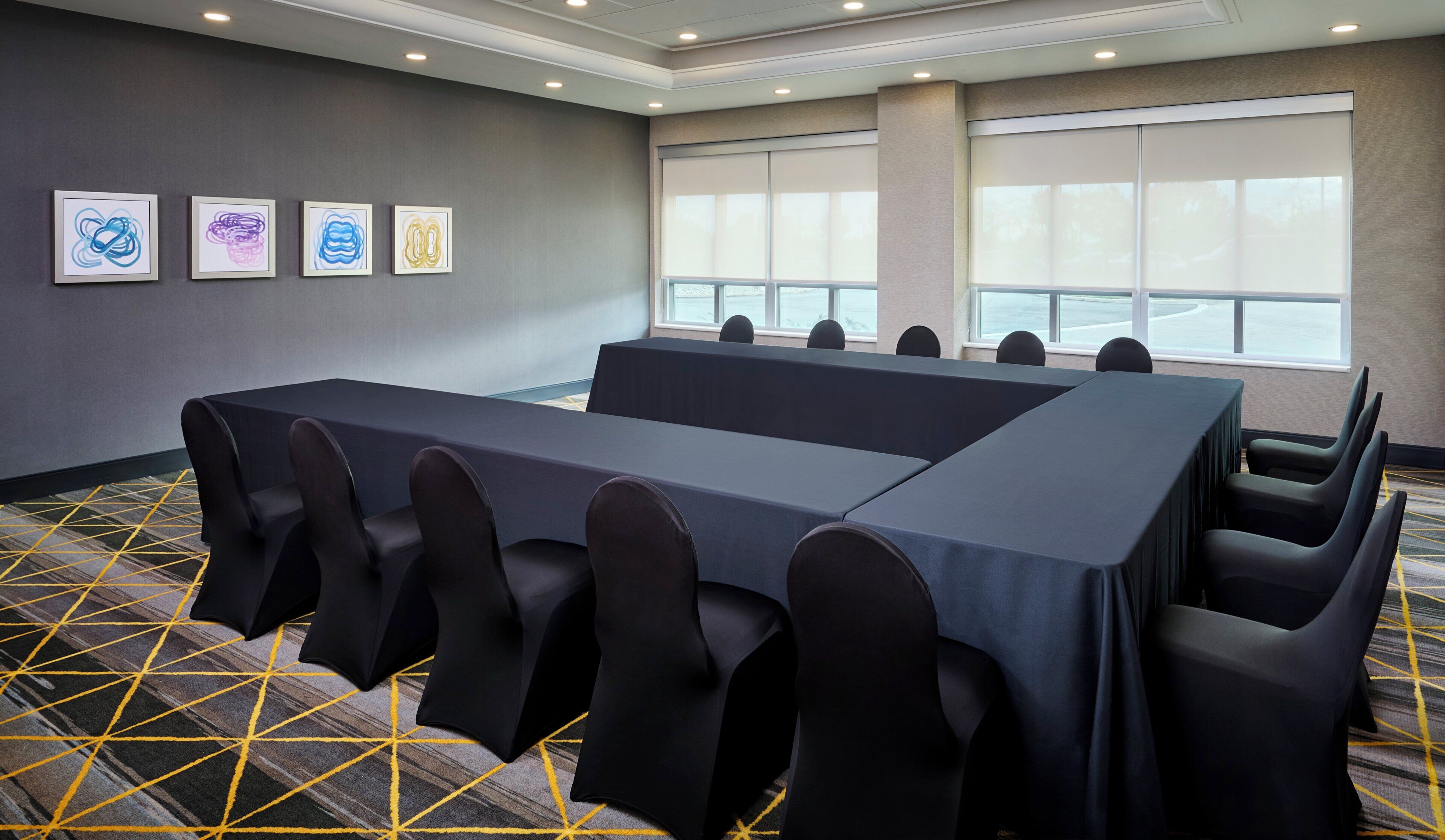 A conference room with a long table and chairs, large windows, and artwork on the wall.
