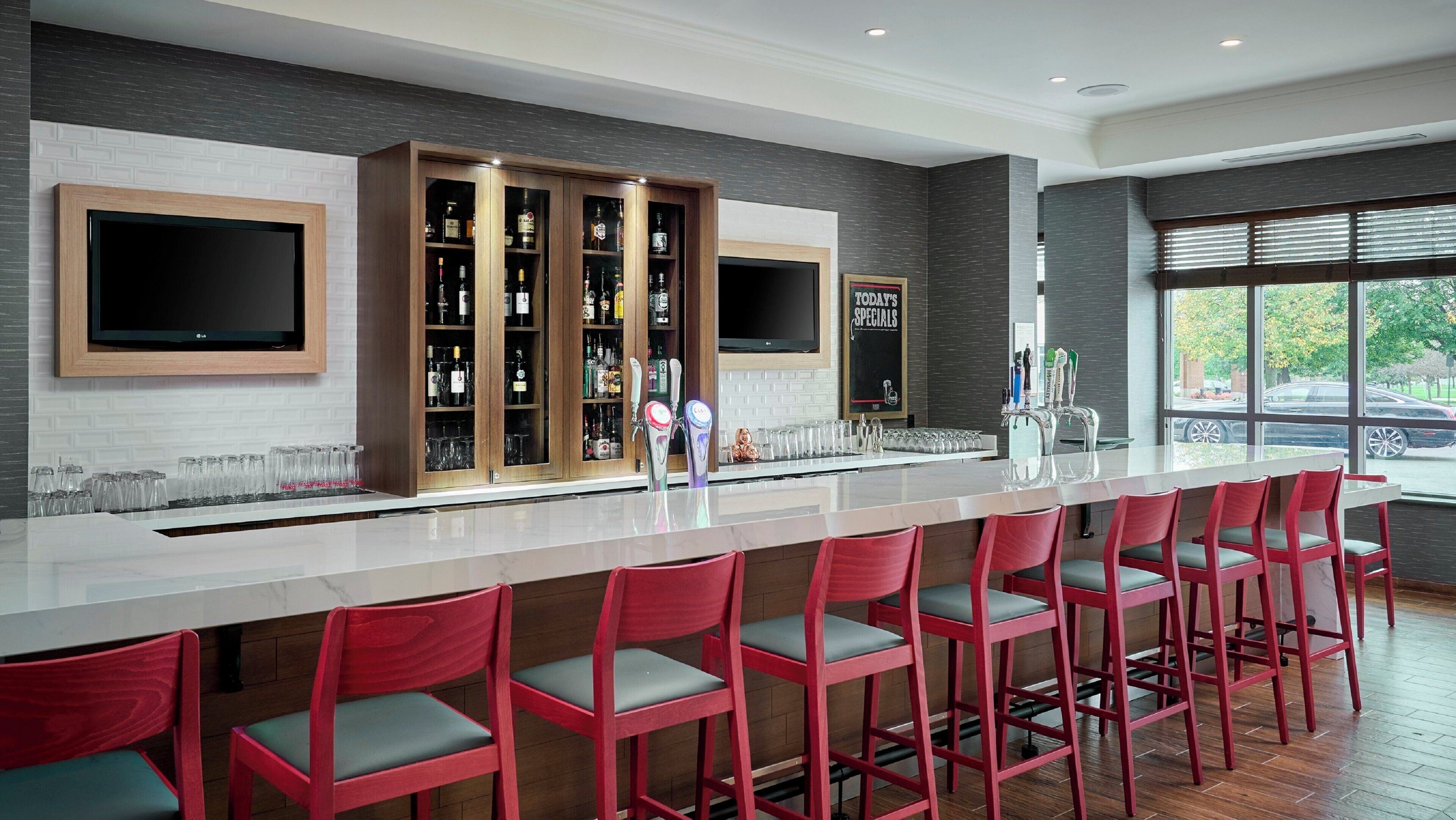 Eine moderne Bar mit einer langen Theke, mehreren Barhocker, einem Fernseher und einem Spirituenschrank.