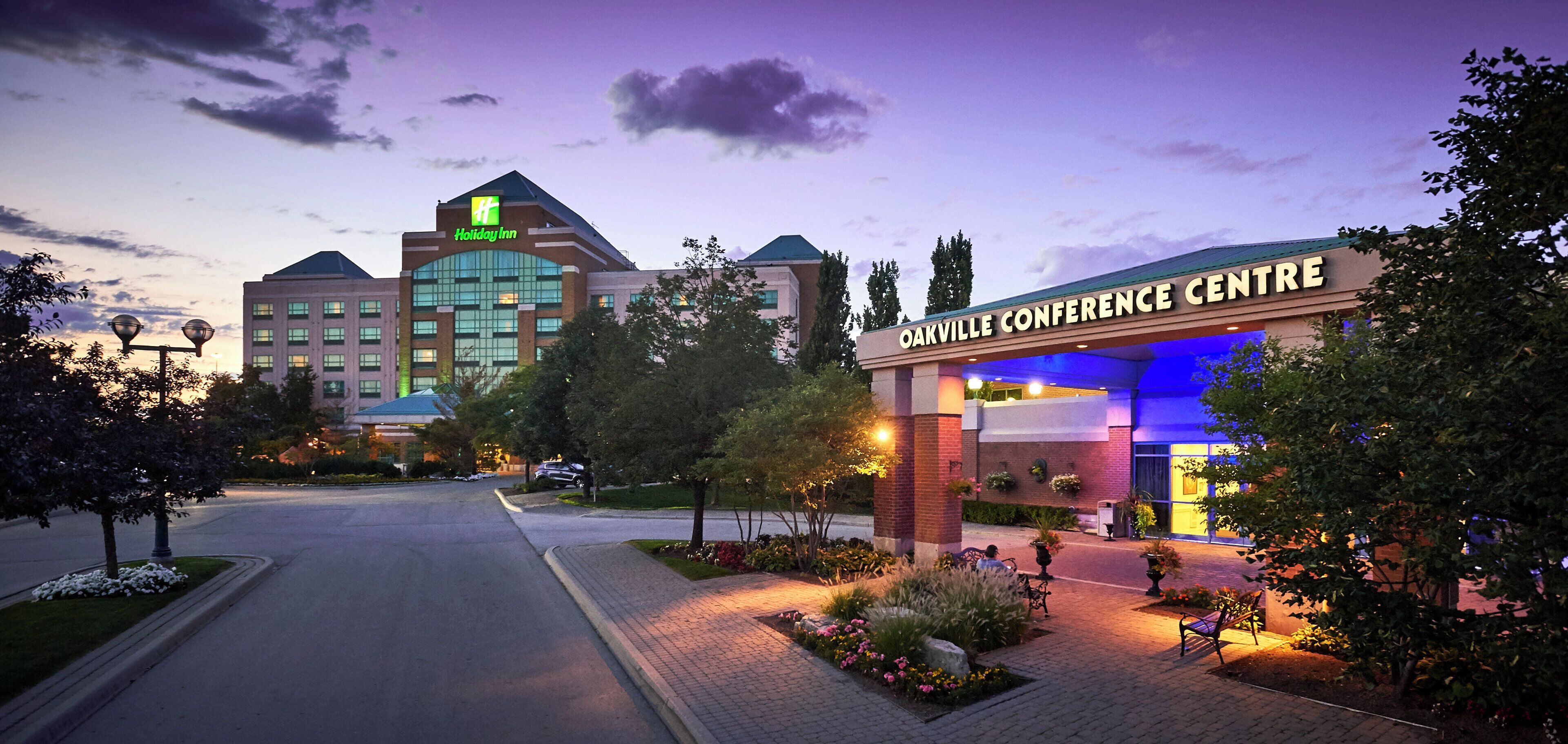 A hotel entrance with a Holiday Inn sign, a conference center, and a landscaped area with benches.