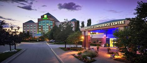 A hotel entrance with a Holiday Inn sign, a conference center, and a landscaped area with benches.