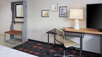 A hotel room with a bed, a desk with a chair, a television, and artwork on the wall.