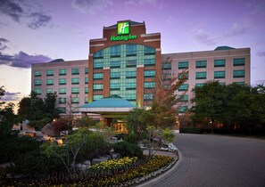 A Holiday Inn hotel with a prominent green logo, a large glass entrance, and a landscaped garden area with yellow flowers. - Holiday Inn Hotel & Suites Oakville @ Bronte by IHG (Oakville)