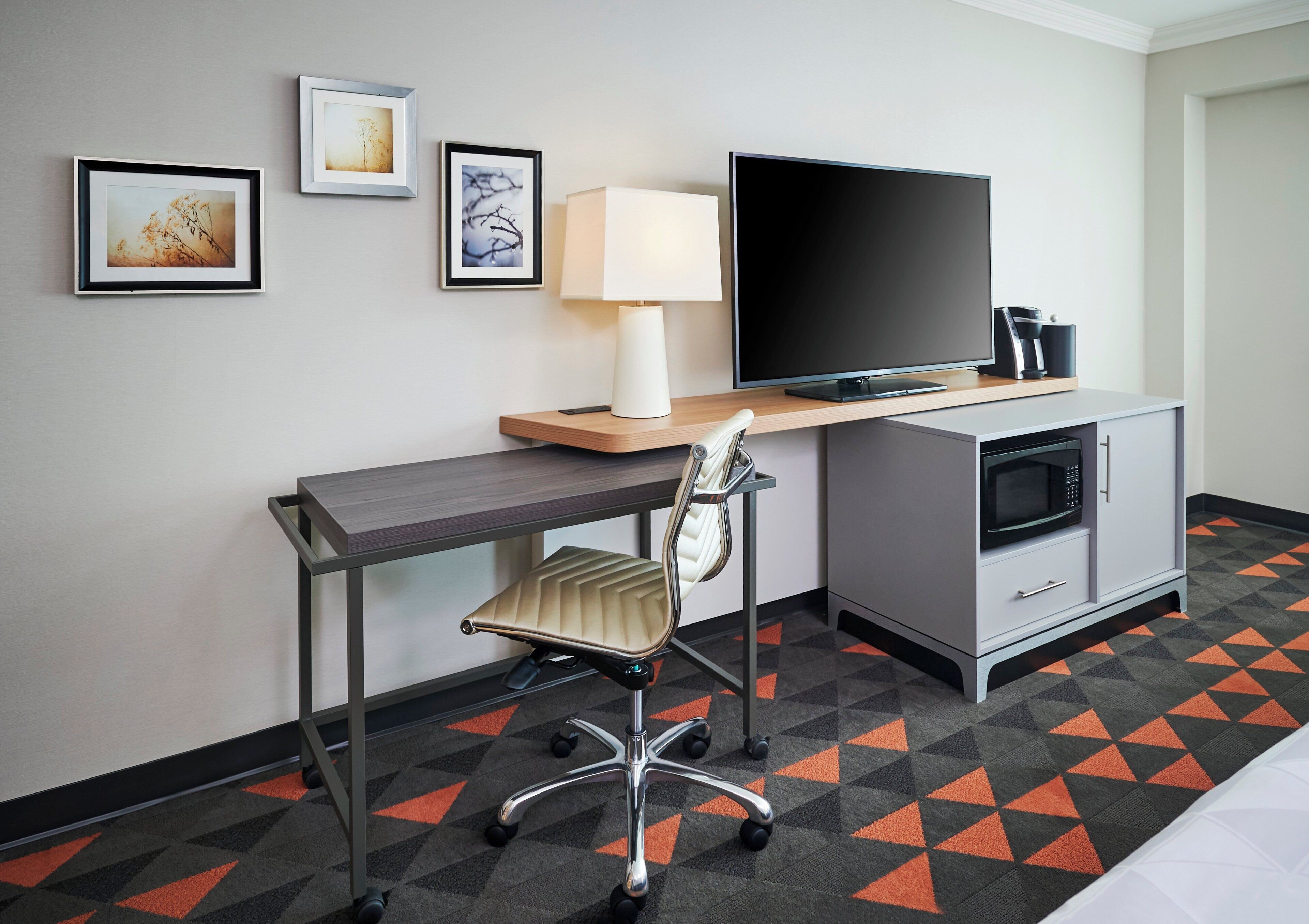 Een hotelkamer met een bureau, stoel, televisie, lamp, magnetron en kast.
