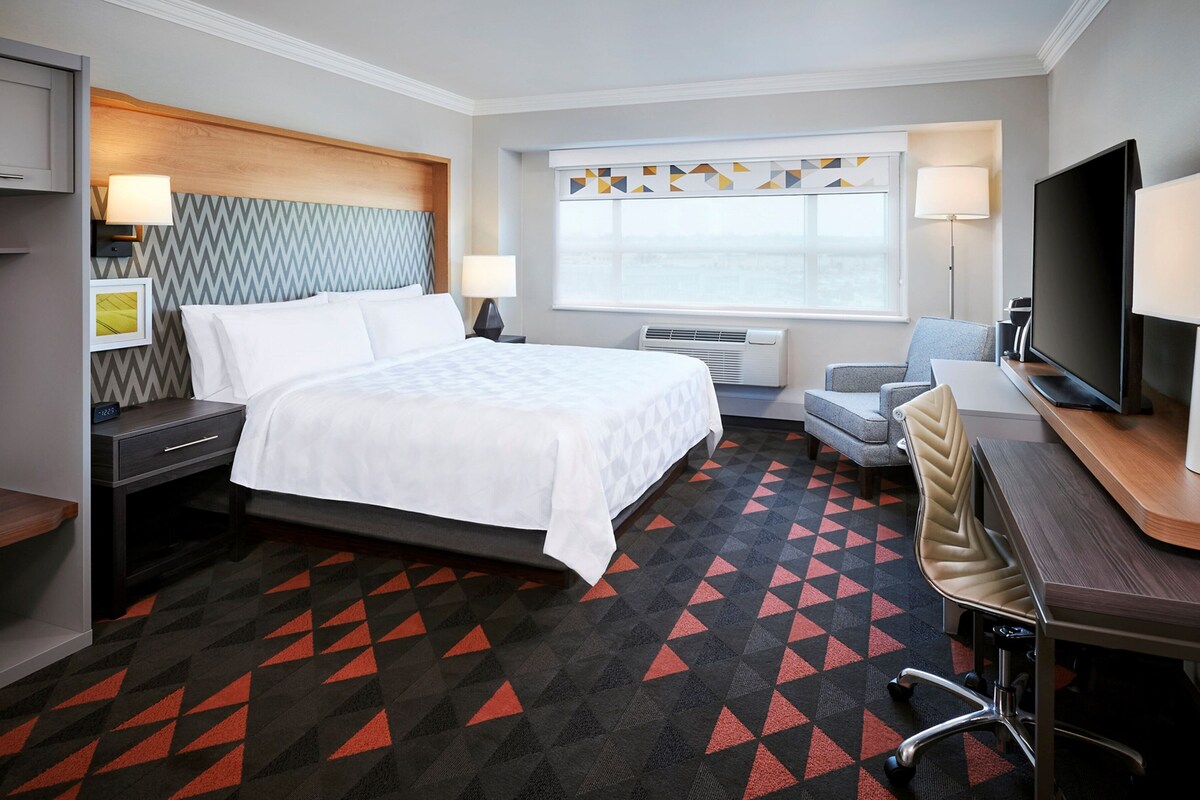 A hotel room with a bed, desk, TV, and a window with a view.