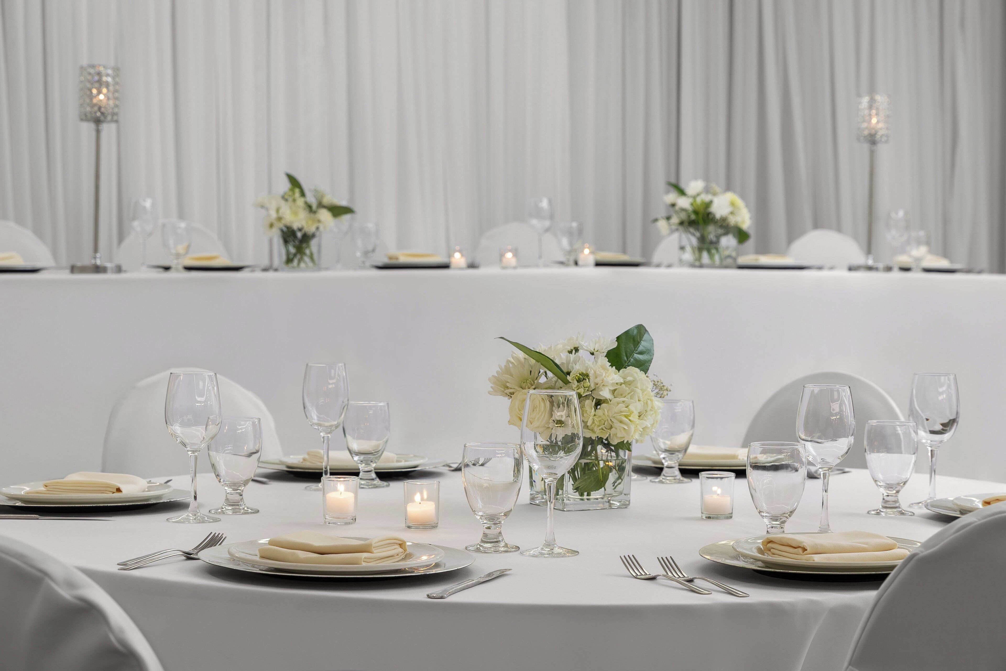 Une table dressée pour un événement formel, avec des nappes blanches, de la verrerie et des bougies.