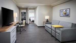 Una habitación de hotel moderna con una televisión de pantalla plana, un sofá, una mesita, un escritorio con lámpara, una silla, un microondas y una cama.