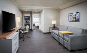A modern hotel room with a flat-screen TV, a sofa, a small table, a desk with a lamp, a chair, a microwave, and a bed. - Holiday Inn Hotel & Suites Oakville @ Bronte by IHG (Oakville)