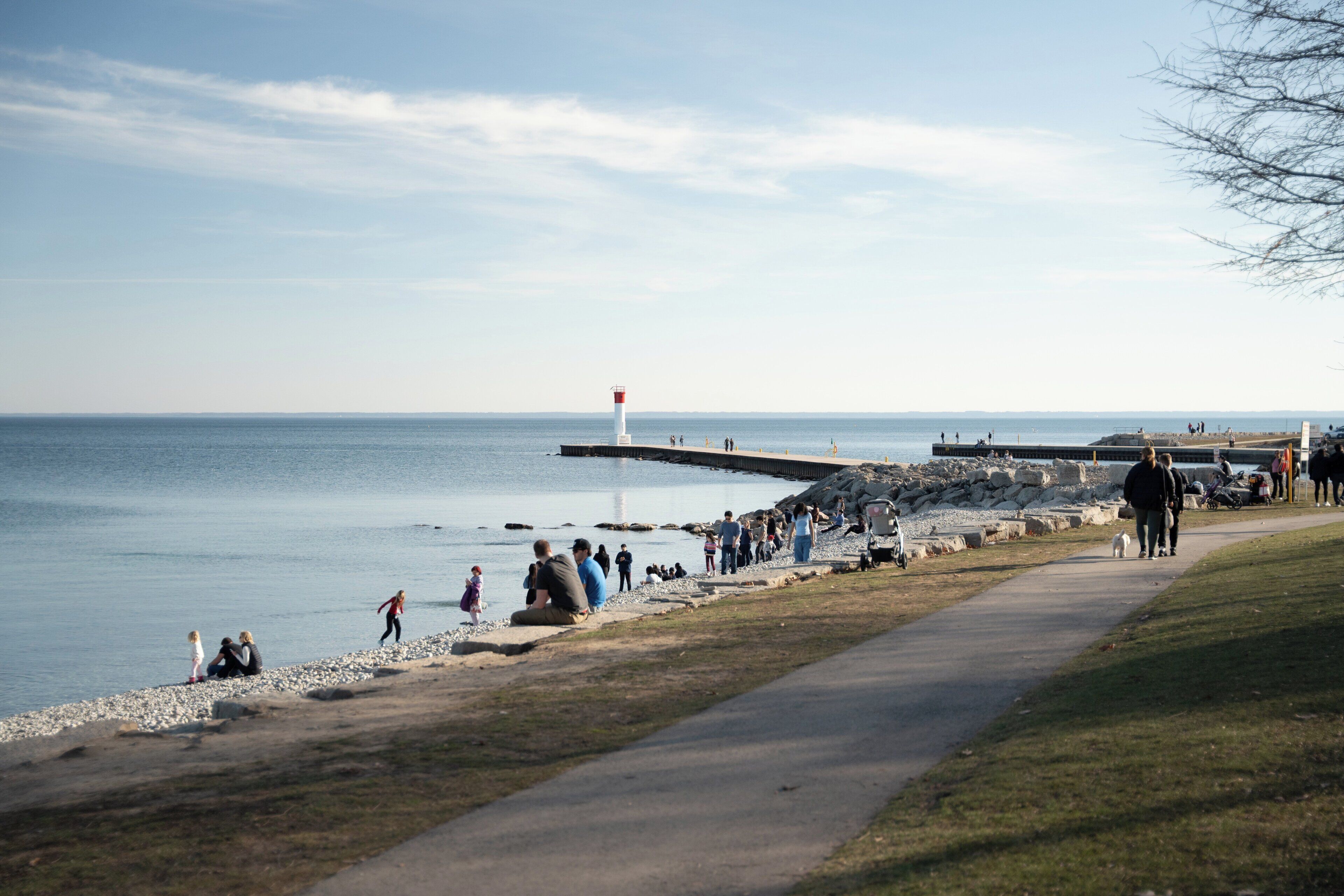 A coastal walkway with a lighthouse, rocky shore, and people walking.