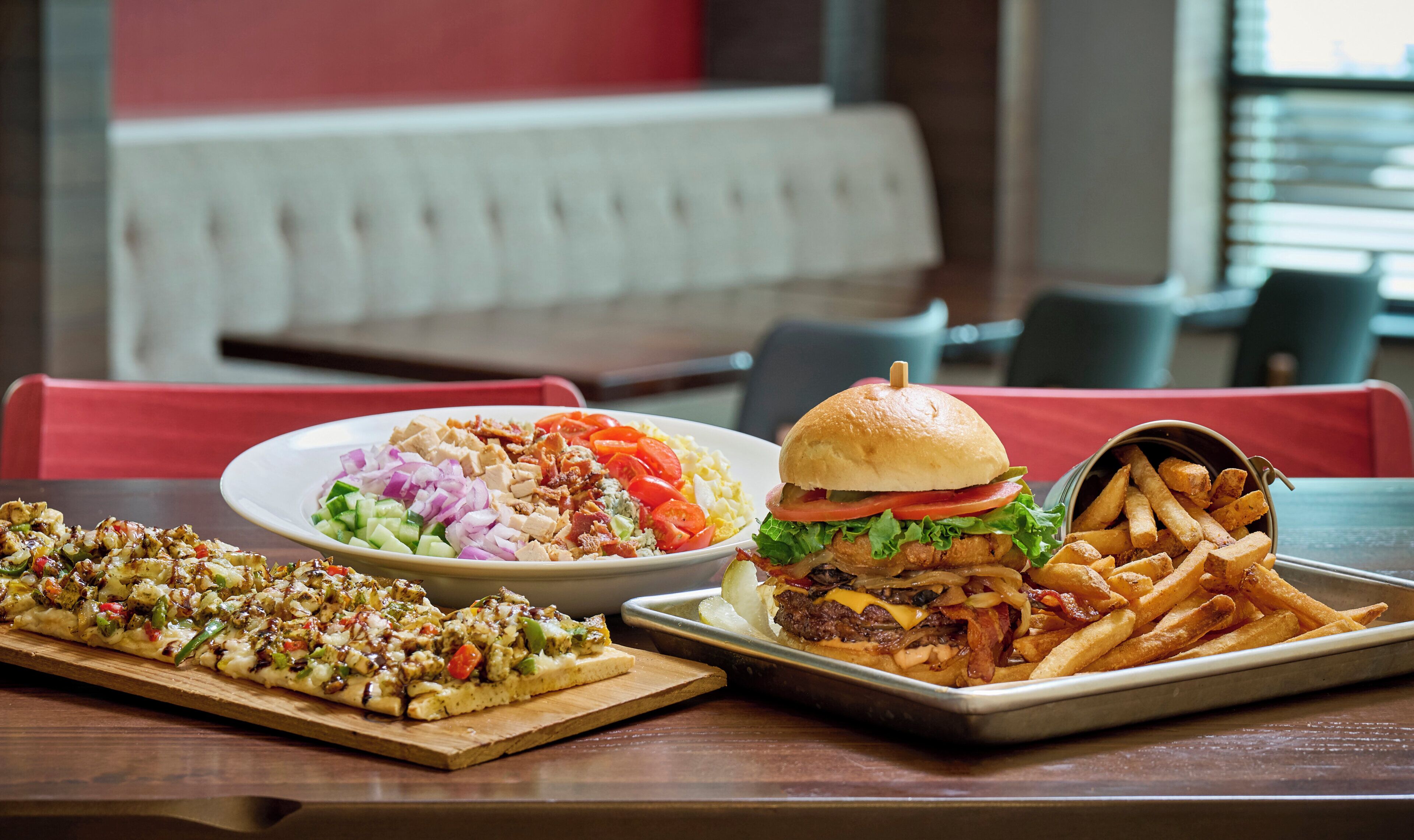 A dining table with a variety of food including a pizza, a salad, a burger, and fries.