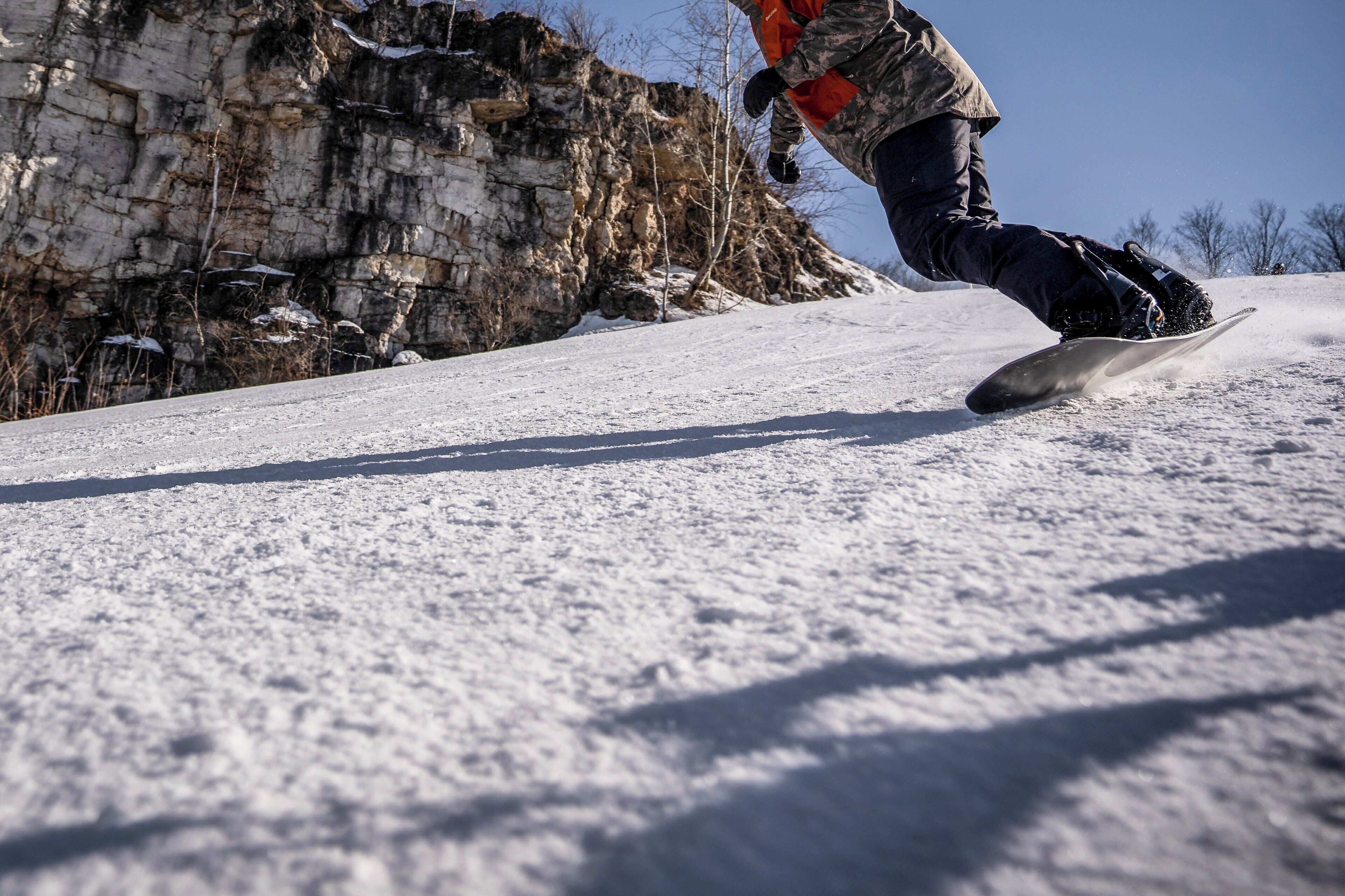Un snowboardeur dévale une pente enneigée, avec des falaises rocheuses en arrière-plan.