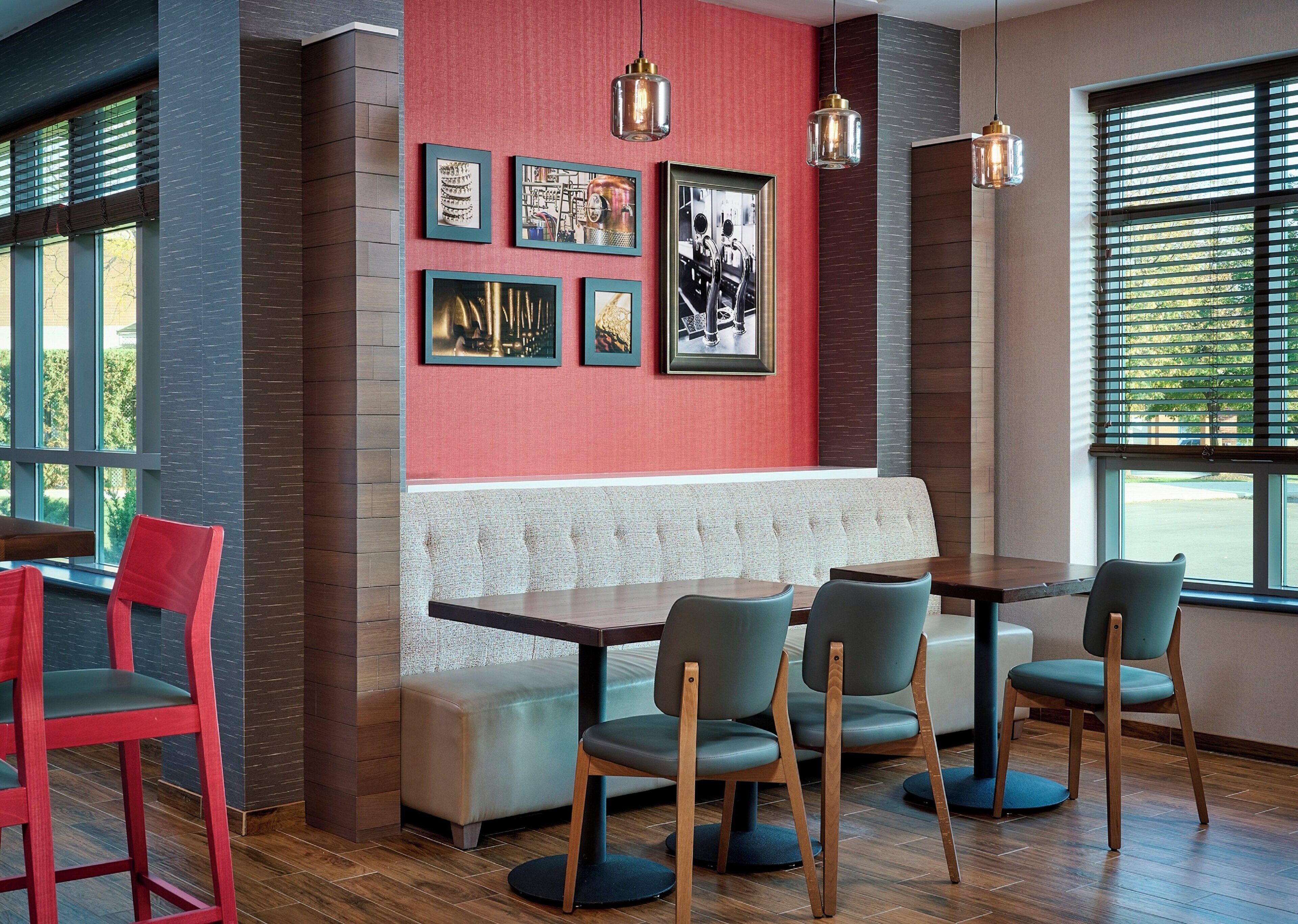 A restaurant interior with a red wall, framed pictures, a wooden bench, and a table with chairs.