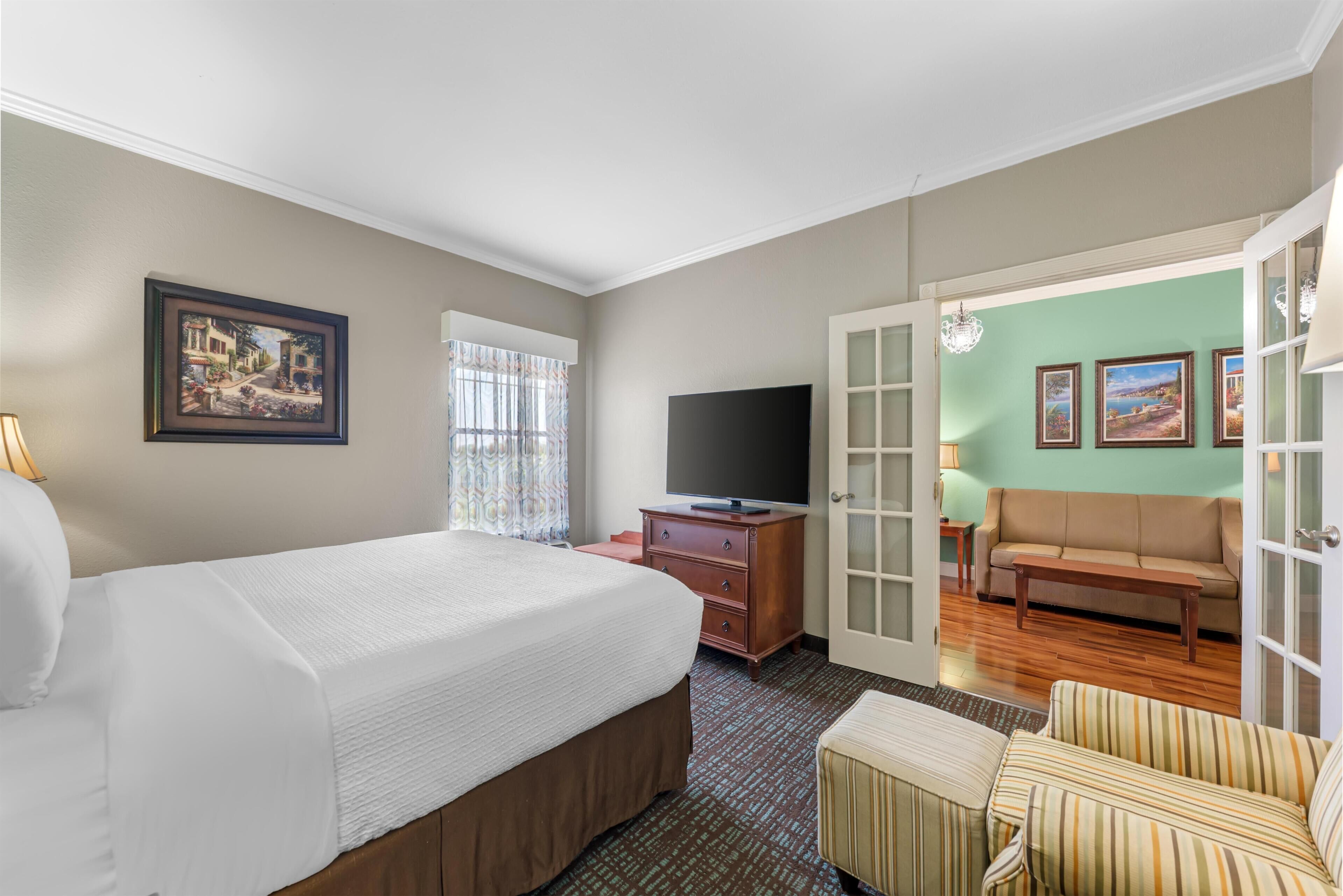 A hotel room with a bed, a TV, a sofa, and a dining table.