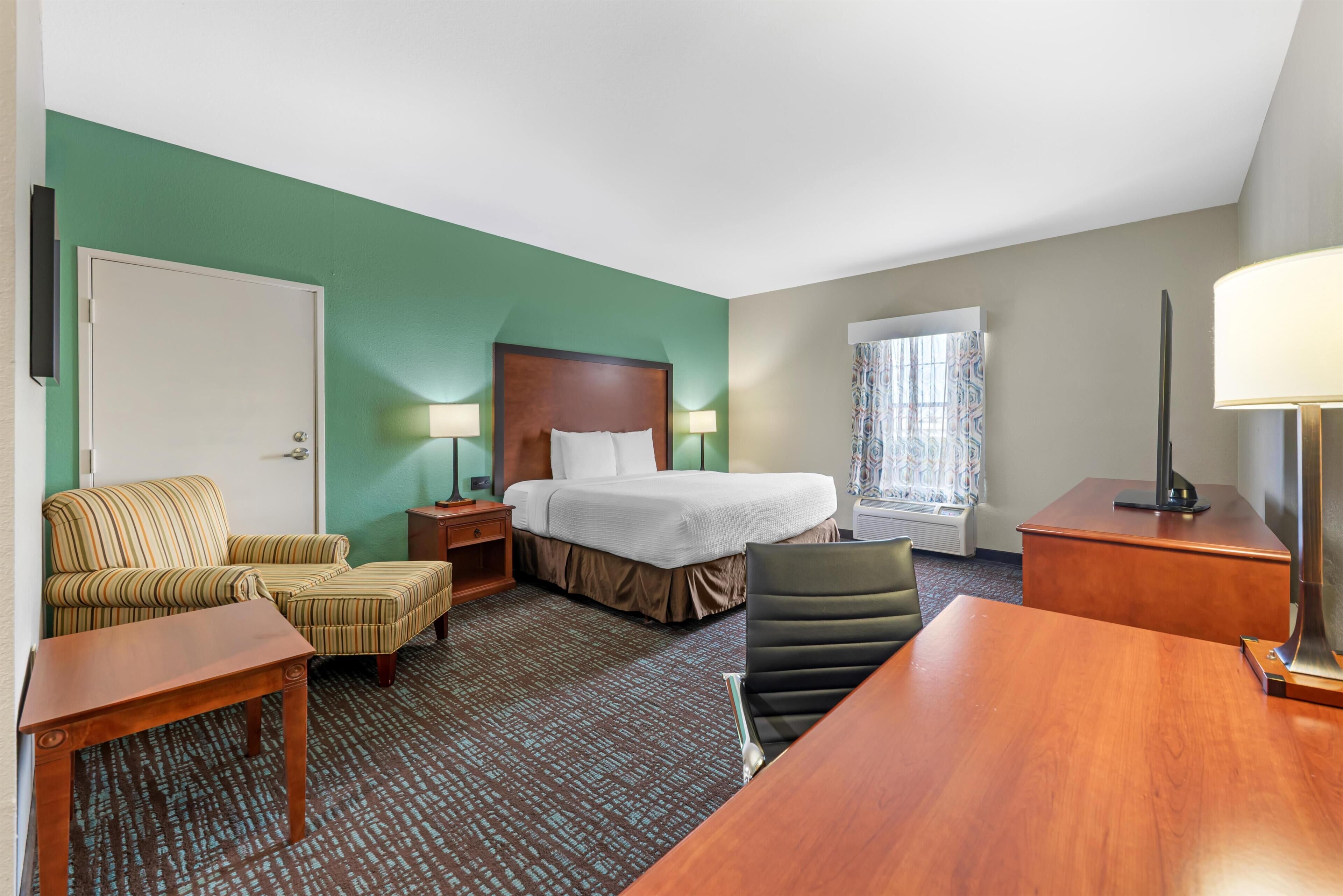 A hotel room with a bed, a desk, a chair, a lamp, and a window with curtains.