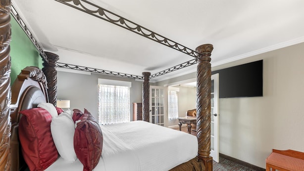 A four-poster bed with a canopy, a wooden bench, a flat-screen TV mounted on the wall, and a door leading to another room. - Best Western Plus Georgetown Inn & Suites (Georgetown)