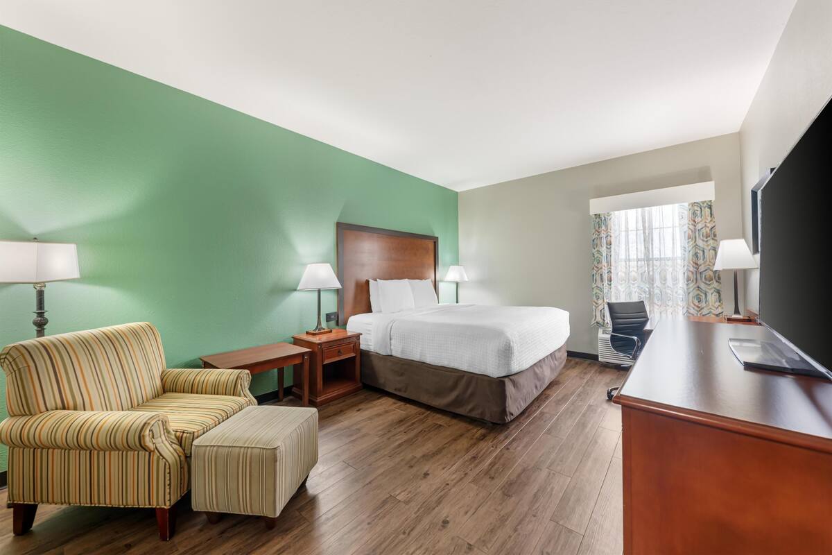 A hotel room with a bed, a chair, a desk, and a television.