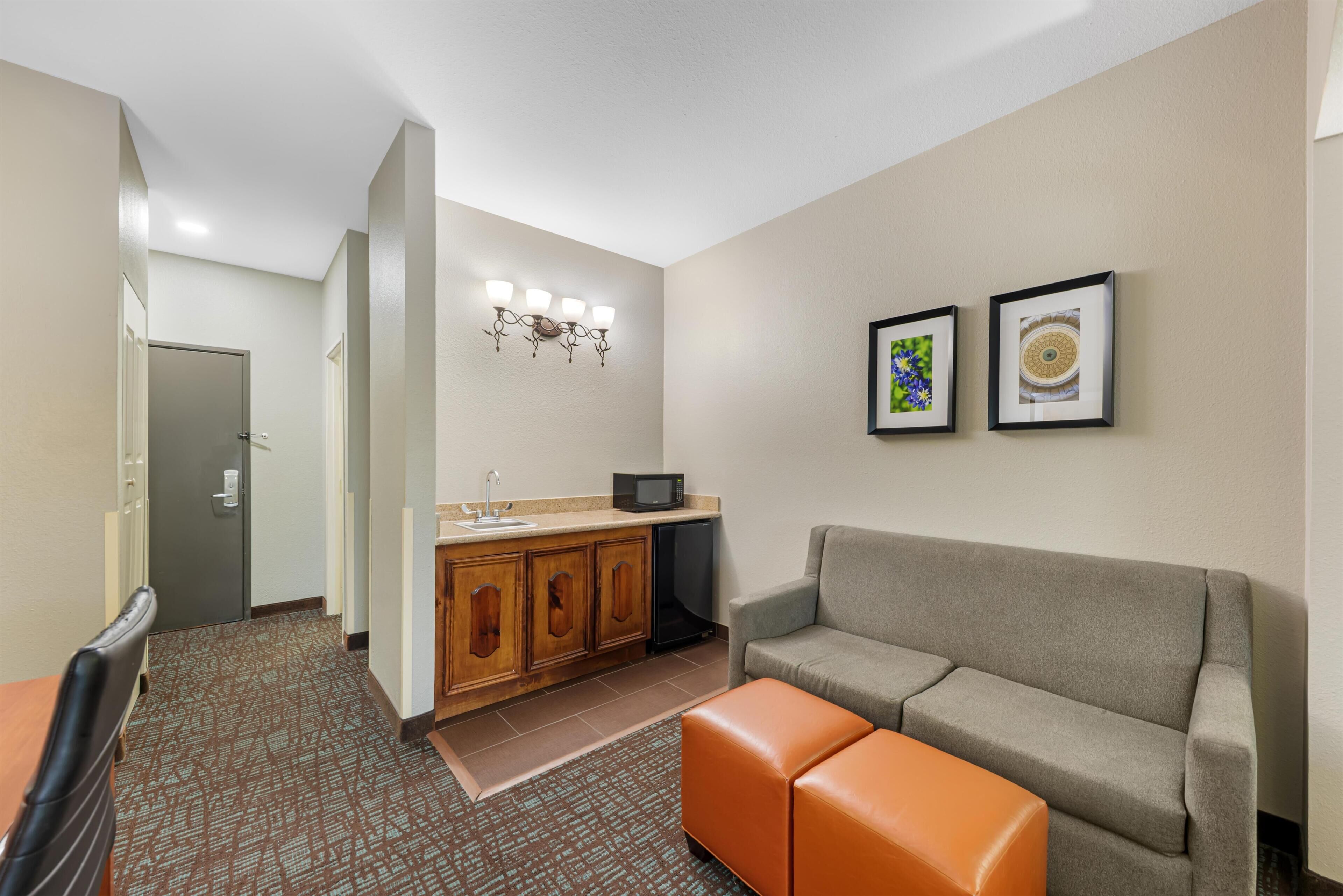 Habitación de hotel con kitchenette, un sofá, una pequeña mesa y una puerta que da a otra habitación.