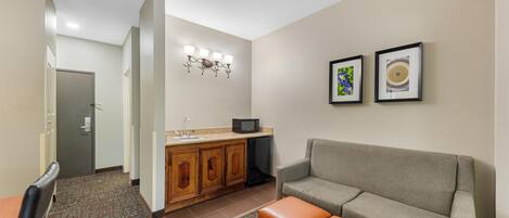 Habitación de hotel con kitchenette, un sofá, una pequeña mesa y una puerta que da a otra habitación.