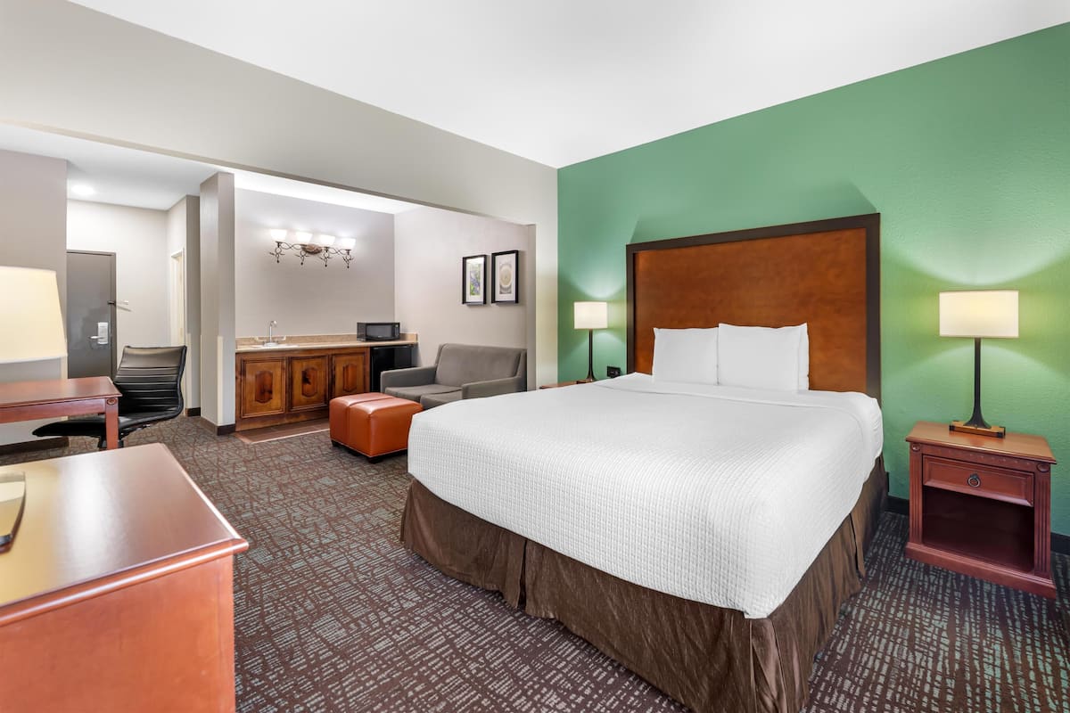 A hotel room with a large bed, a desk, a chair, a sofa, a desk lamp, and a nightstand.
