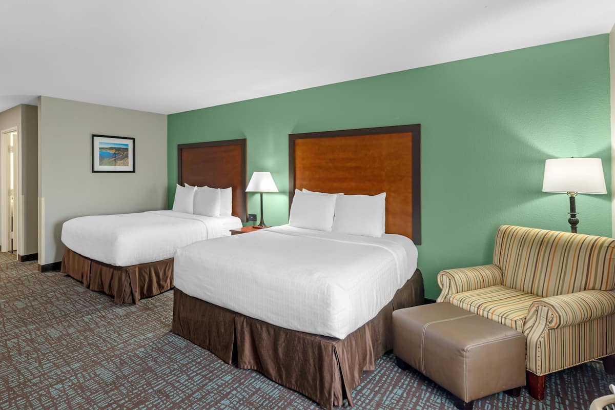 A hotel room with two beds, a sofa, a chair, and a lamp.