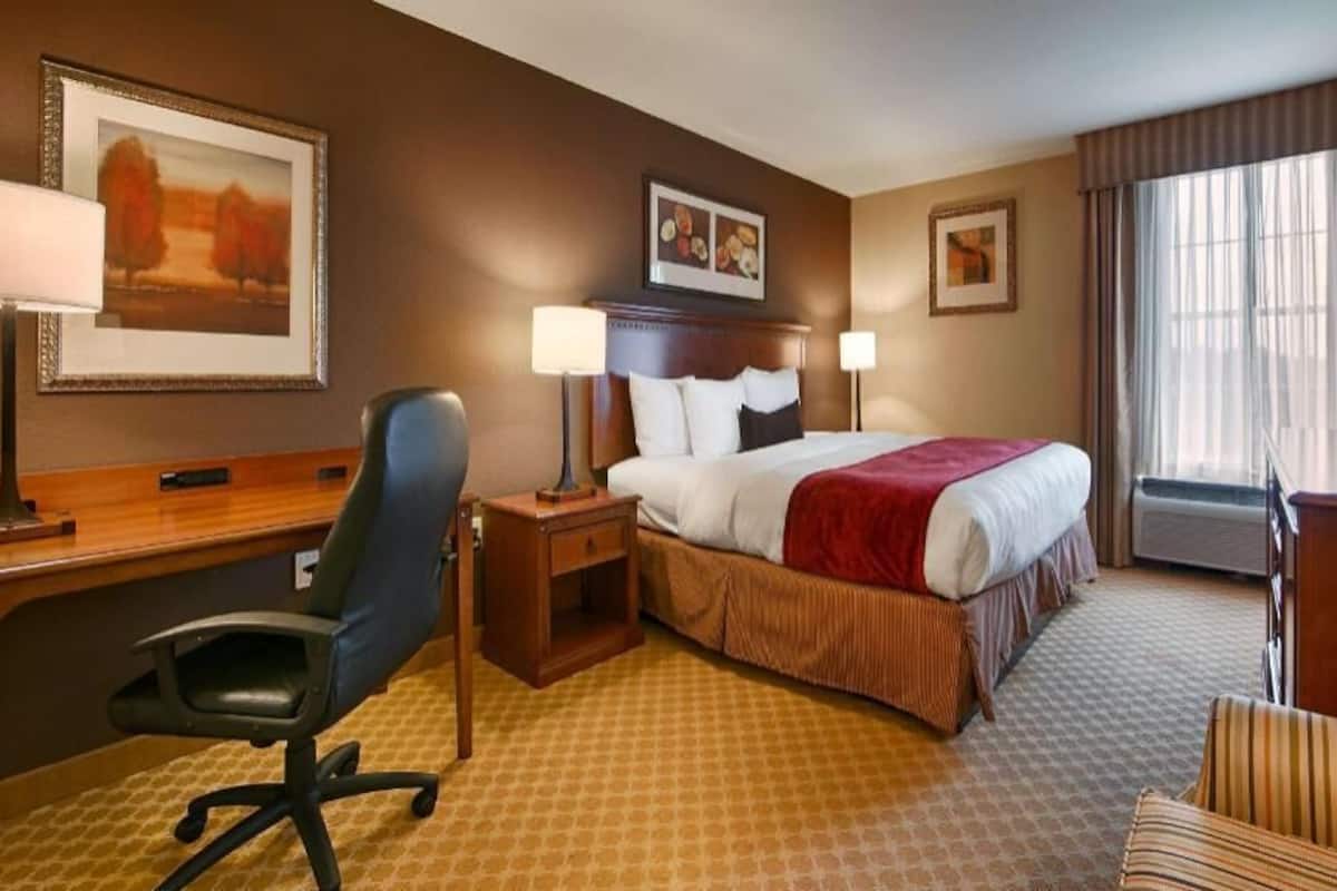 A hotel room with a bed, desk, chair, TV, and artwork on the walls.