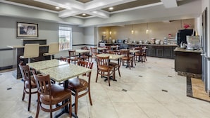 A spacious dining area with multiple tables and chairs, a kitchen area with appliances, and a framed picture on the wall. - Best Western Plus Georgetown Inn & Suites (Georgetown)