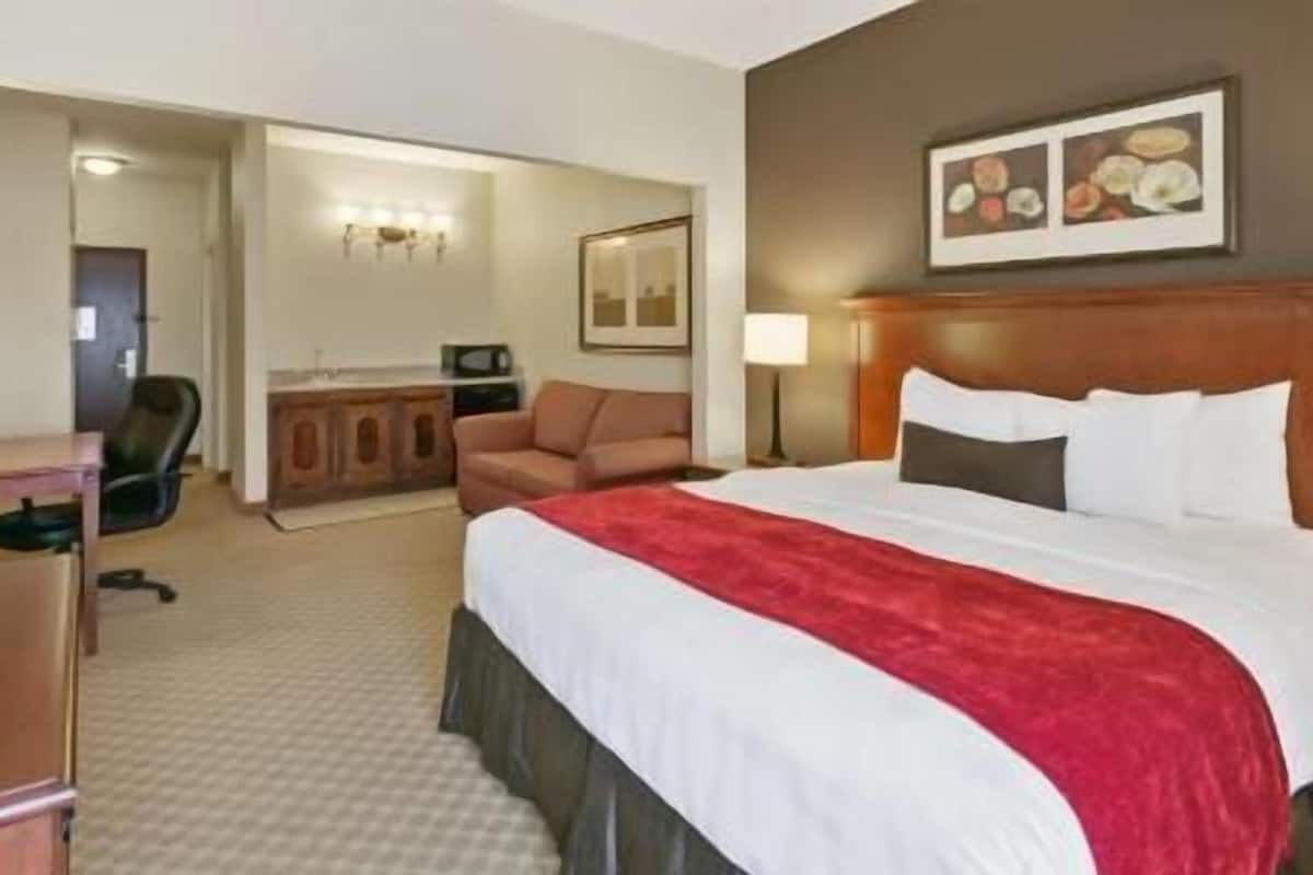 A hotel room with a bed, a desk, a chair, a microwave, a television, and a door leading to another room.