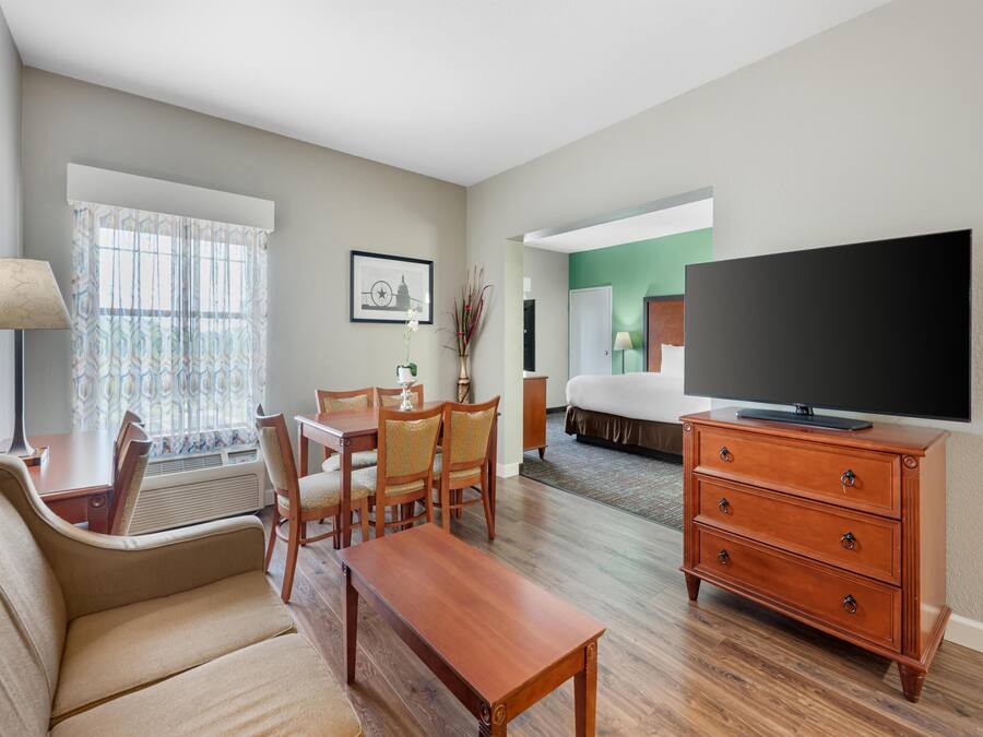 A hotel room with a living area, a dining table, a sofa, a TV, and a bed.