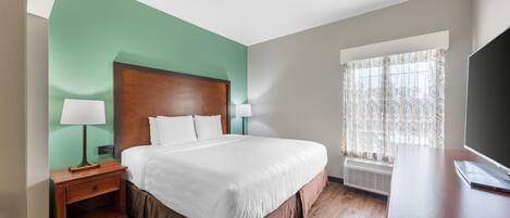 Una habitación de hotel con cama, mesita de noche, lámpara, televisor y ventana con cortinas.