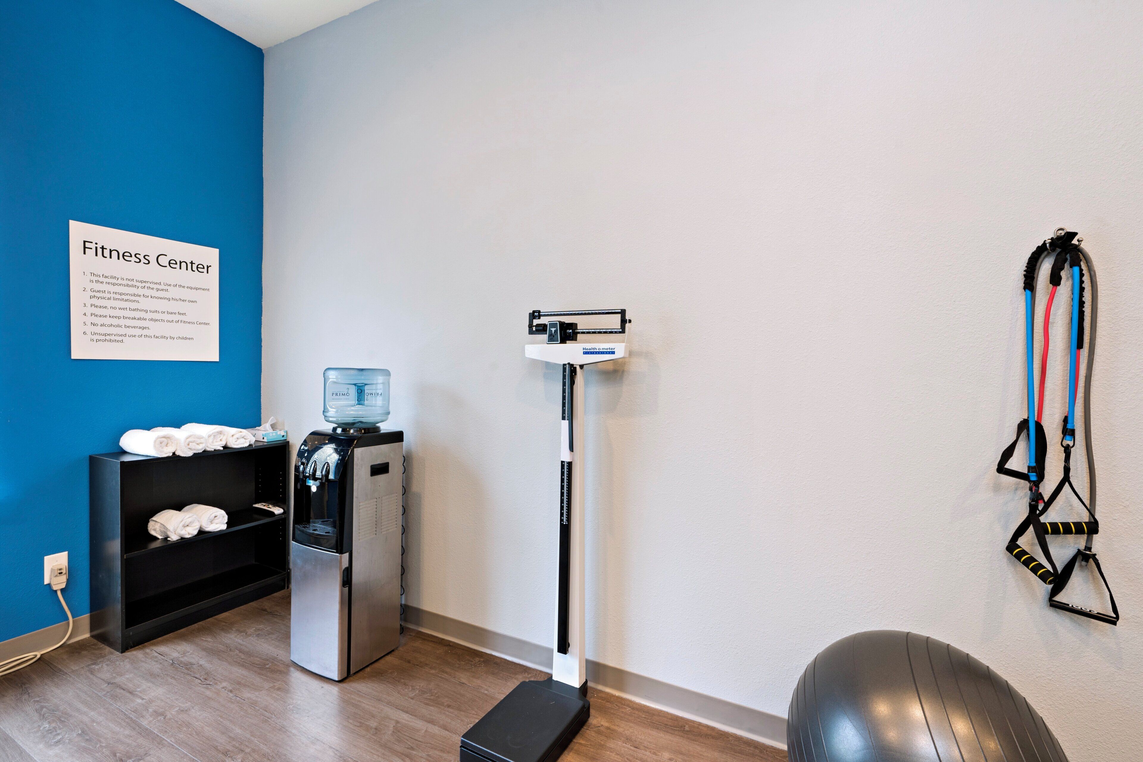 Ein Fitnessstudio mit Wasserspender, Trainingsgeräten und einem Schild mit Regeln.