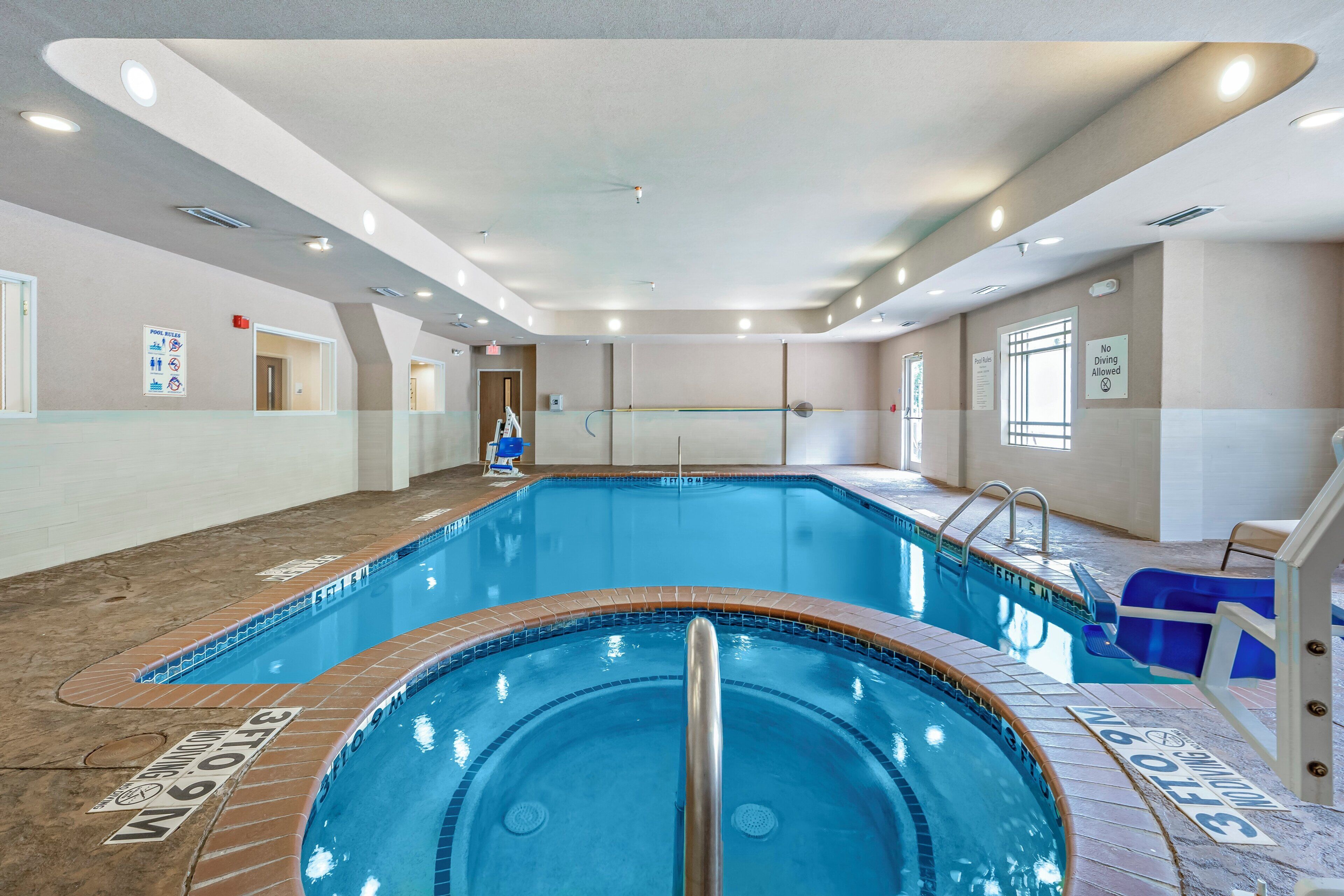 Une piscine intérieure avec des panneaux indiquant clairement les règles d’utilisation, un plongeoir et un poste de surveillance pour le sauveteur.
