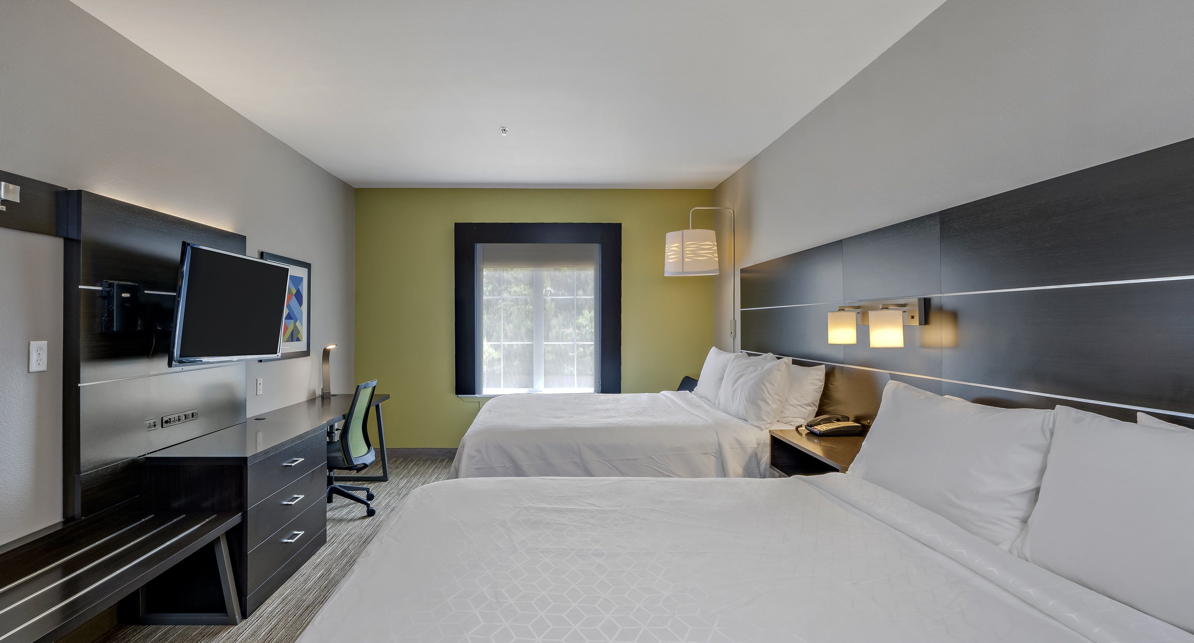 A hotel room with two beds, a desk with a TV, a chair, and a window with blinds.