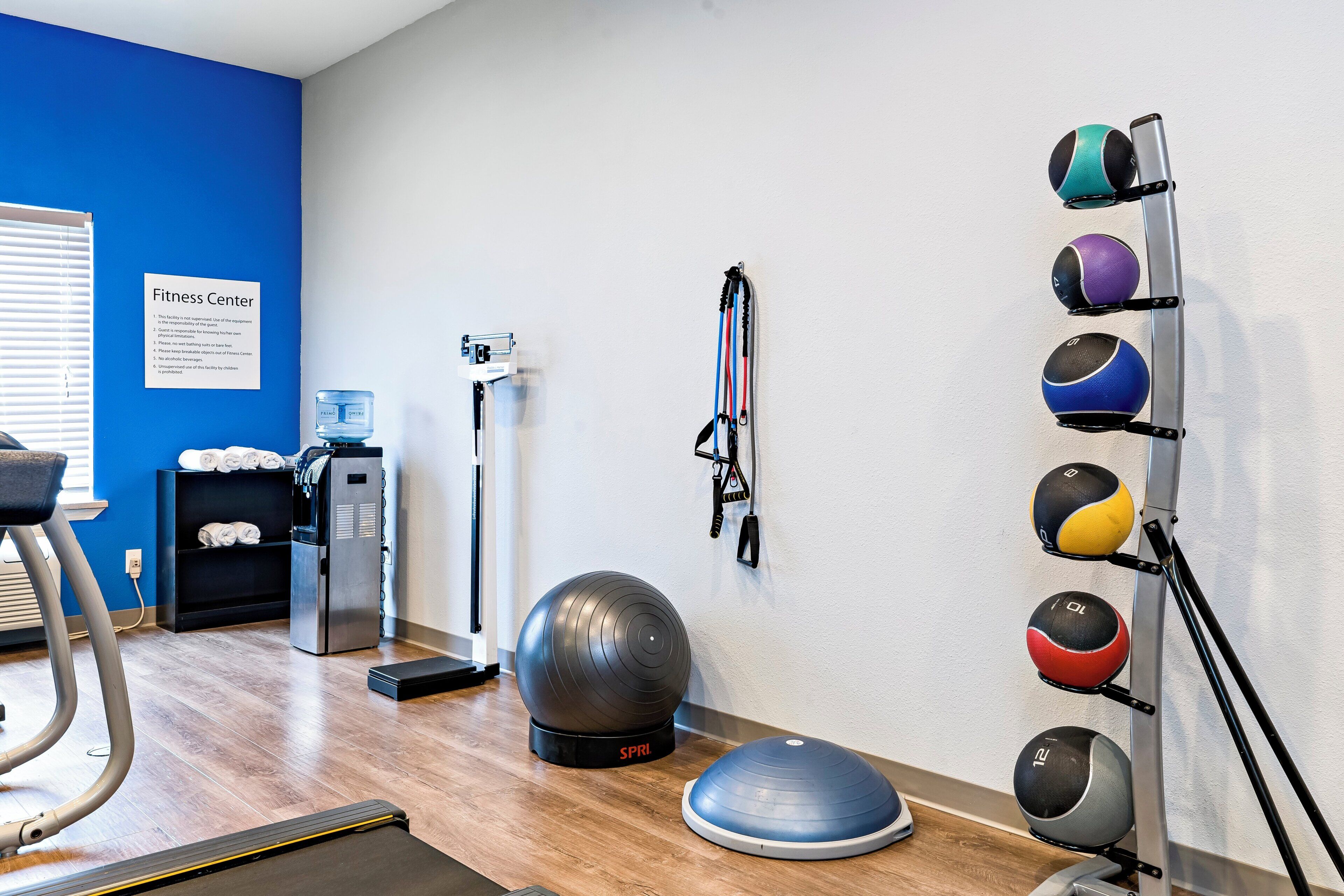 A fitness center with exercise equipment, a water dispenser, and a sign listing rules.