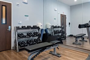 Et fitnesscenter med træningsudstyr, herunder håndvægte, bænke og et løbebånd.