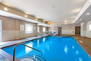 En inomhuspool med klart vatten, en hoppställning och en loungehörna med stolar.
