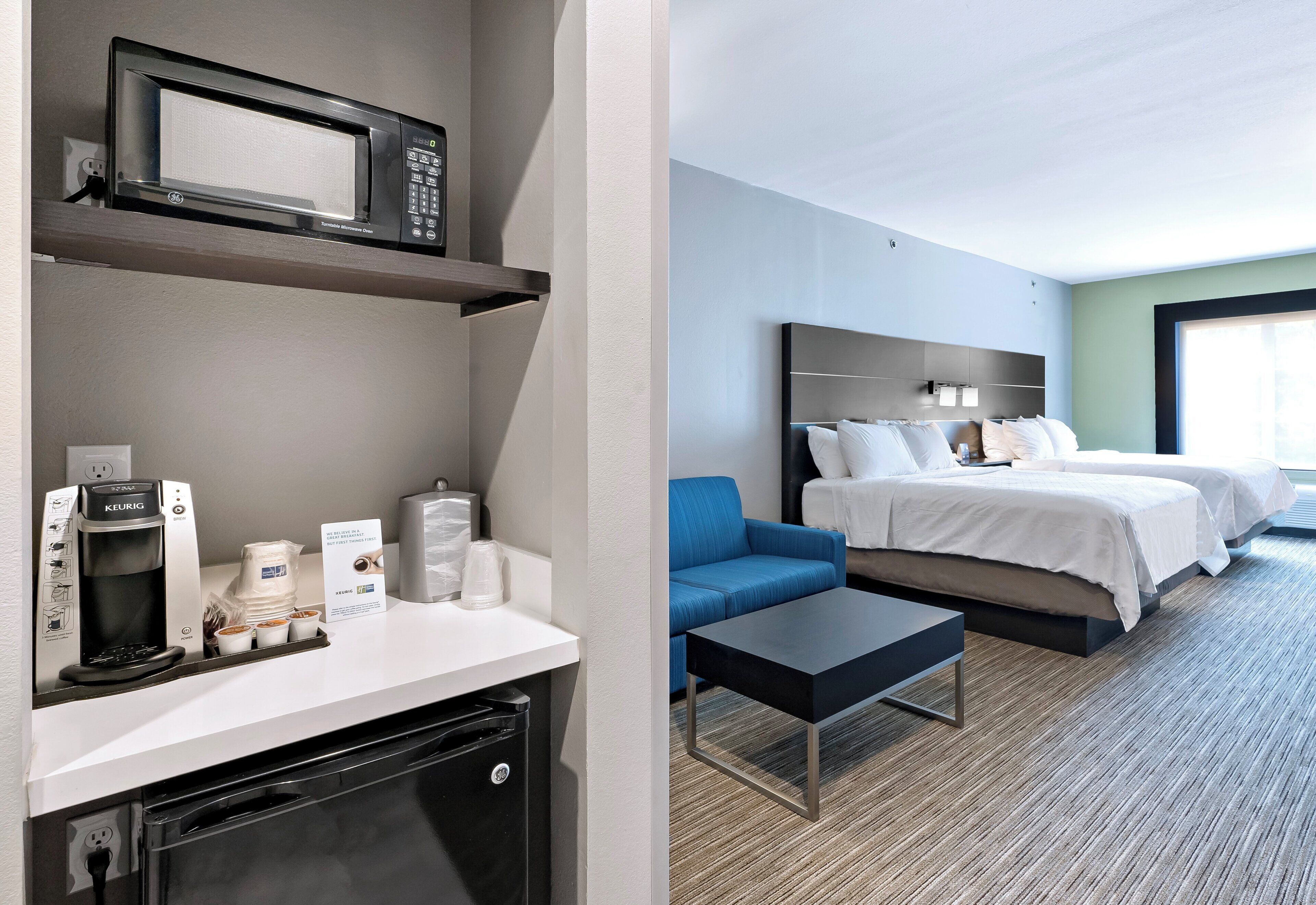 Habitación de hotel con kitchenette, una cama, un sofá azul y vista a la ciudad.