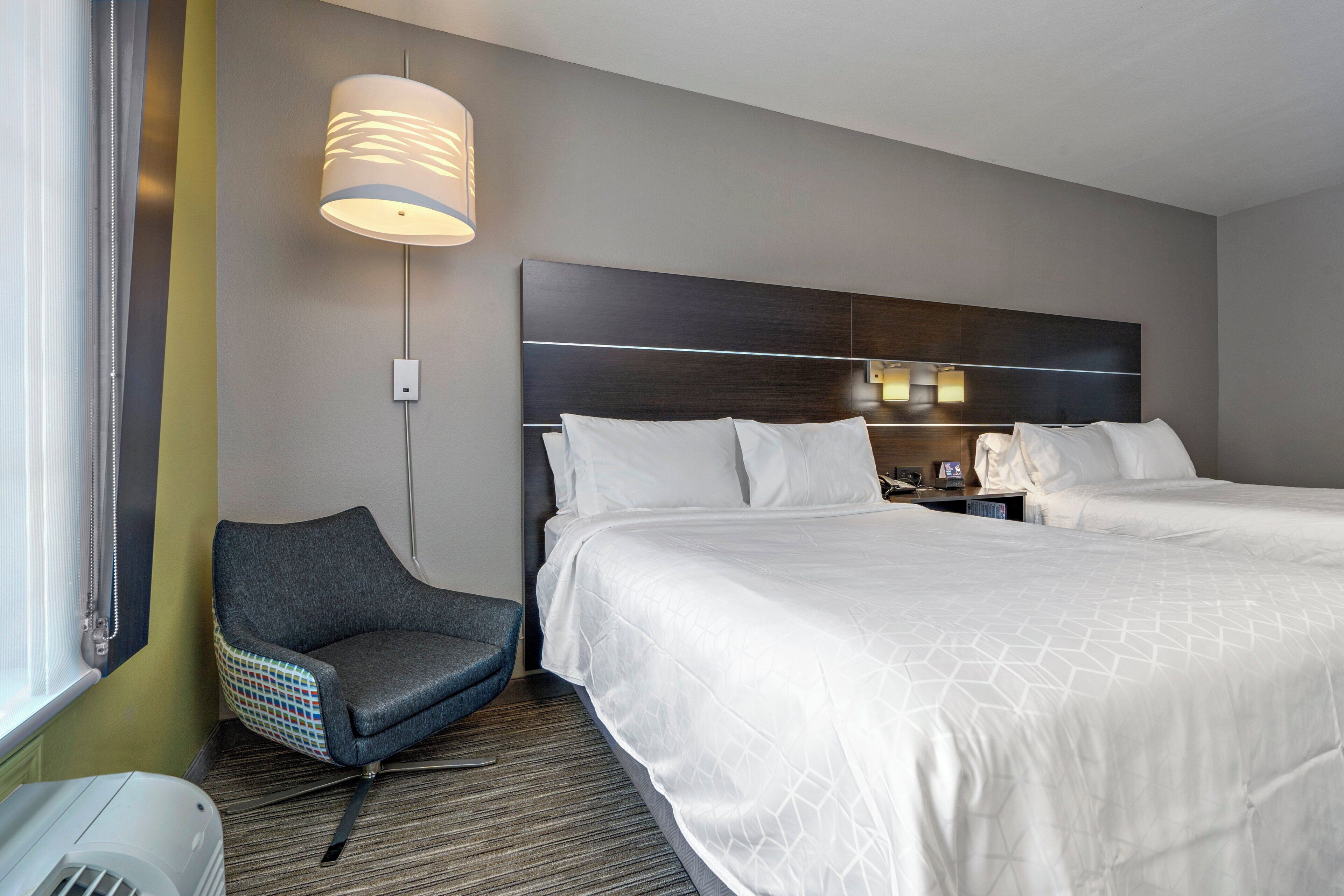 A hotel room with a large bed, a chair, a lamp, and a wall-mounted light fixture.
