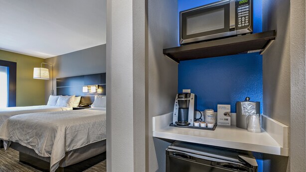 Quarto de hotel com cama, mesa de cabeceira, cafeteira, micro-ondas e mini-geladeira.