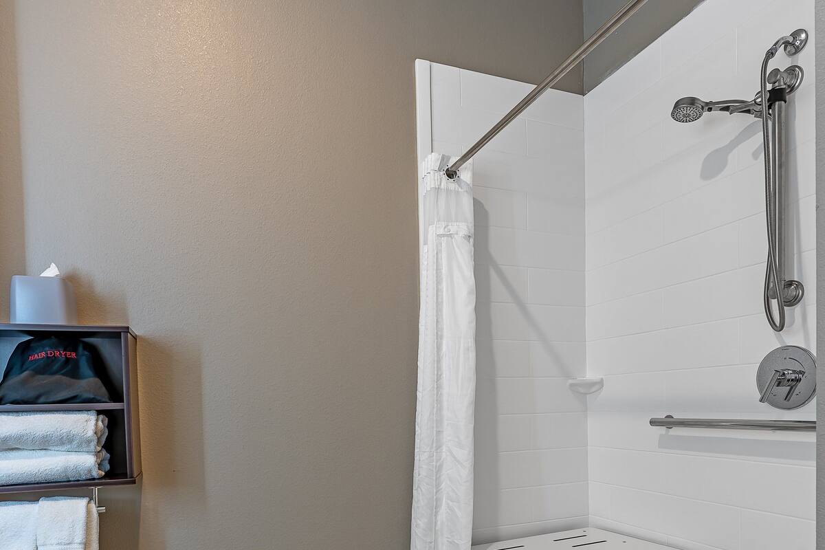 A modern shower area with a glass door, a towel rack with folded towels, and a handheld showerhead.