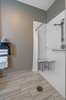 Un área de ducha moderna con puerta de cristal, un perchero con toallas dobladas y un cabezal de ducha de mano.
