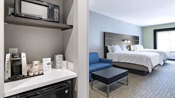 Quarto de hotel com cozinha compacta, uma cama, sofá azul e uma pequena mesa.