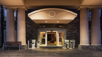 Enter through a grand archway supported by large columns, into a warmly lit interior with a welcoming atmosphere.