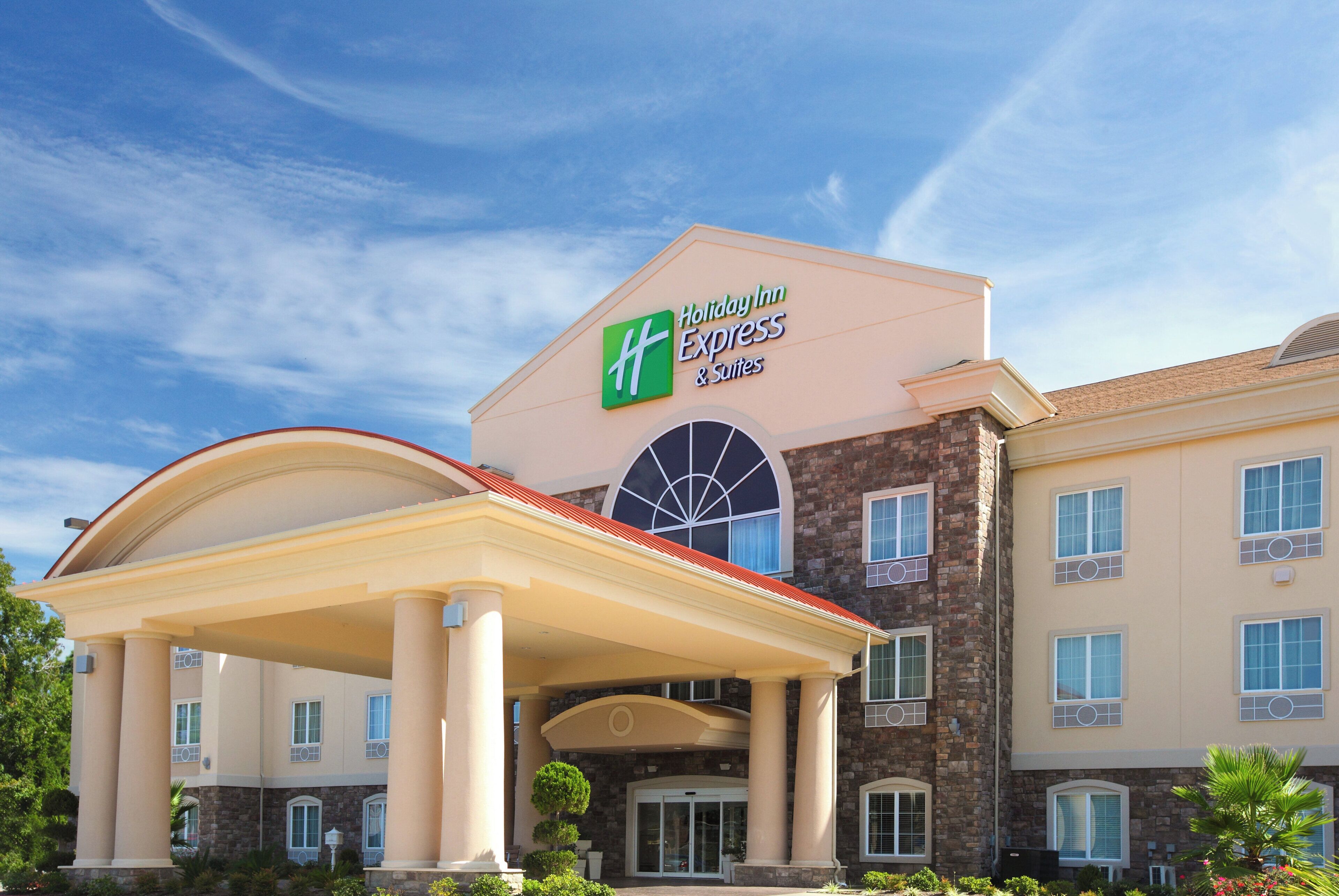 A Holiday Inn Express & Suites building with a prominent entrance, a covered patio area, and a clear blue sky in the background.