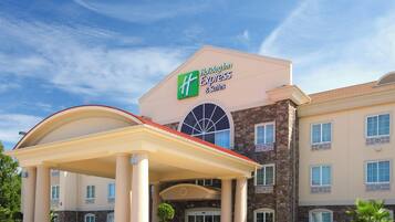 A Holiday Inn Express & Suites building with a prominent entrance, a covered patio area, and a clear blue sky in the background.