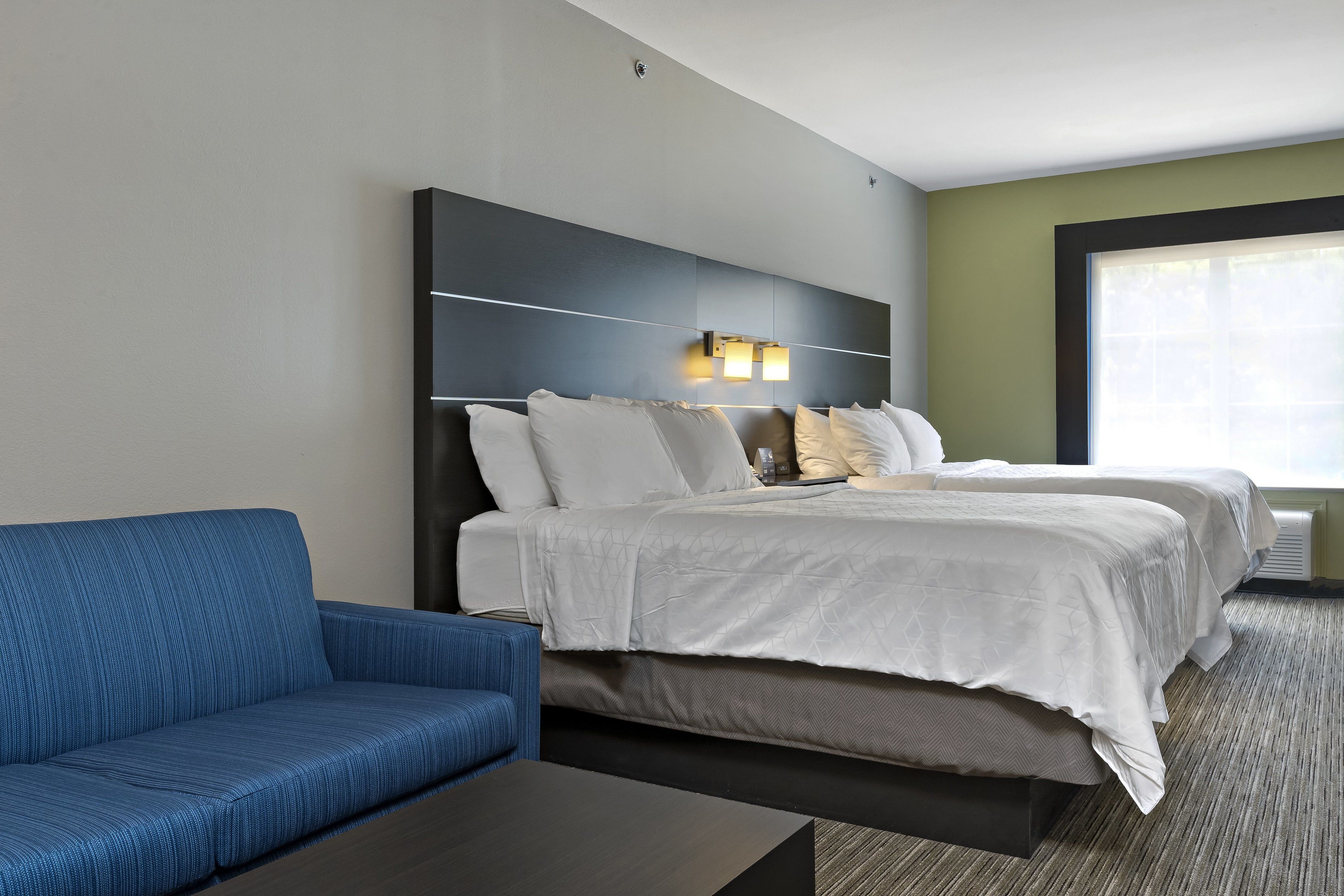 A hotel room with a large bed, a blue sofa, and a small table.