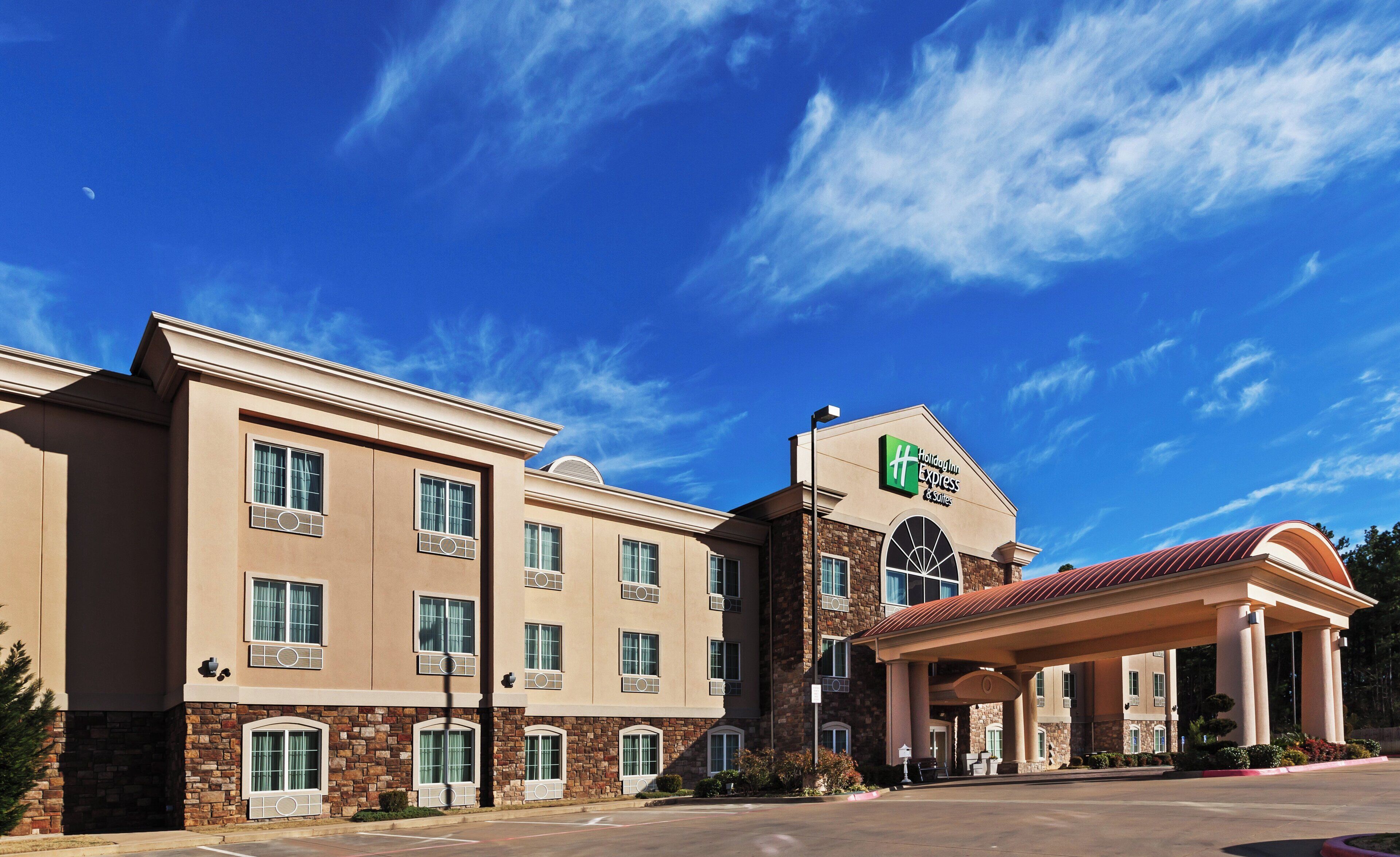 Un hôtel Holiday Inn Express & Suites, avec un bâtiment à deux étages, une entrée couverte et un ciel d’un bleu éclatant.