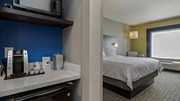 A hotel room with a bed, a desk with a coffee maker, a microwave, and a window with blinds.