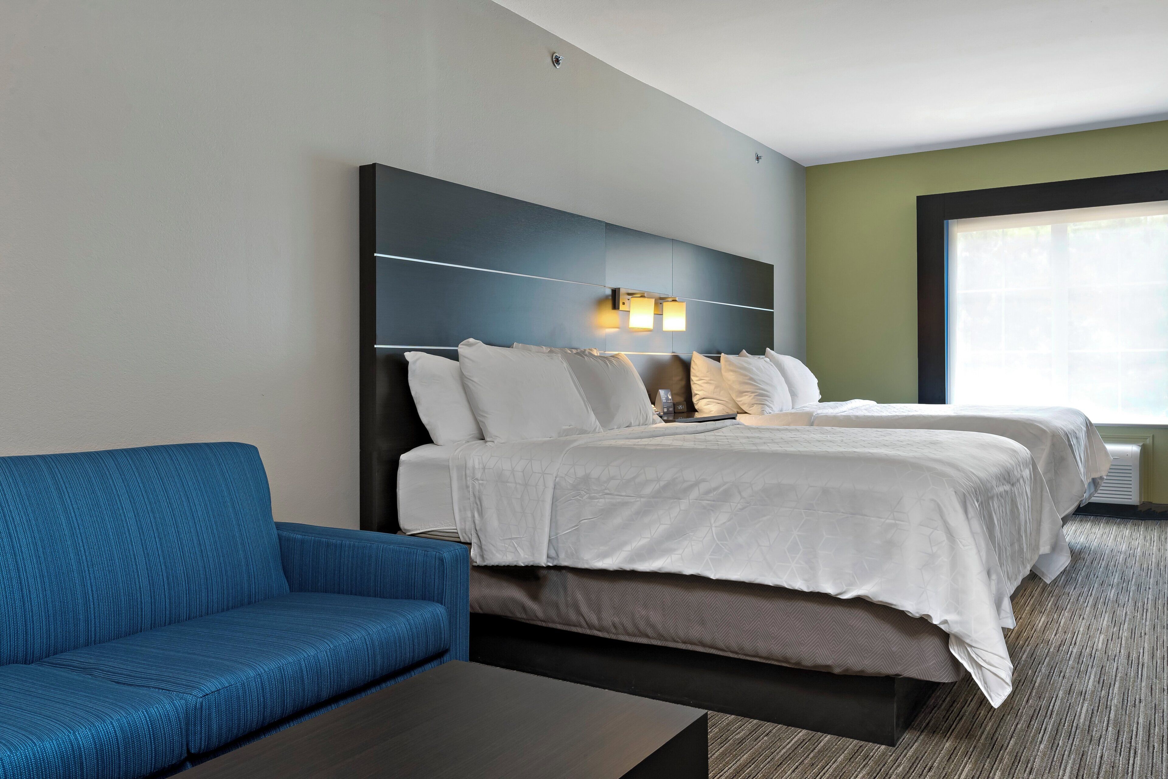 A hotel room with a bed, a blue sofa, a dark coffee table, and a large window.